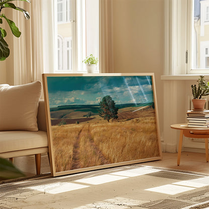 Framed landscape print of golden fields placed on a shelf beside a small plant.
