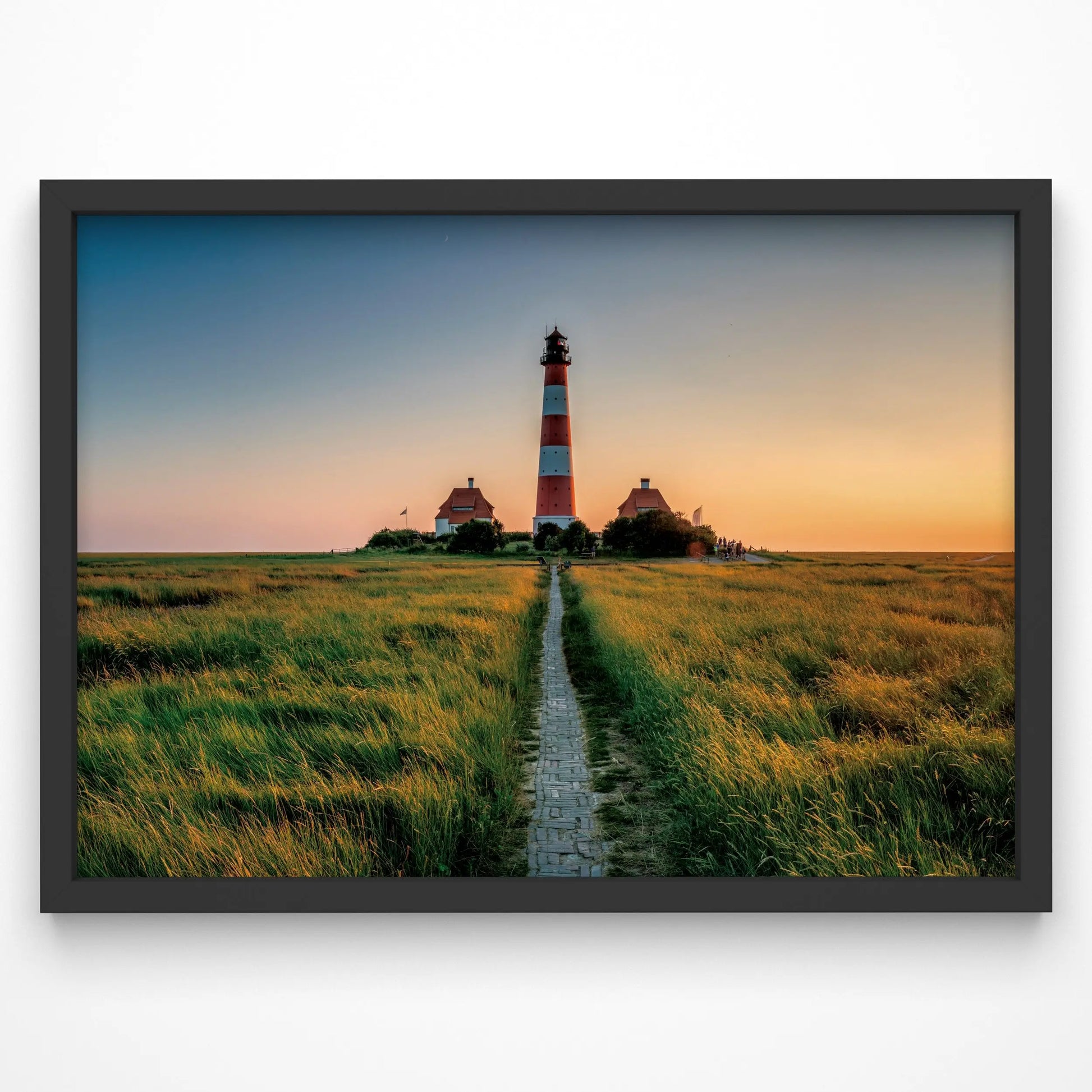 A striking lighthouse print featuring a red-and-white striped lighthouse standing tall at the end of a narrow brick path. The golden hues of sunset cast a warm glow over the grassy coastal landscape, creating a timeless and inviting scene.