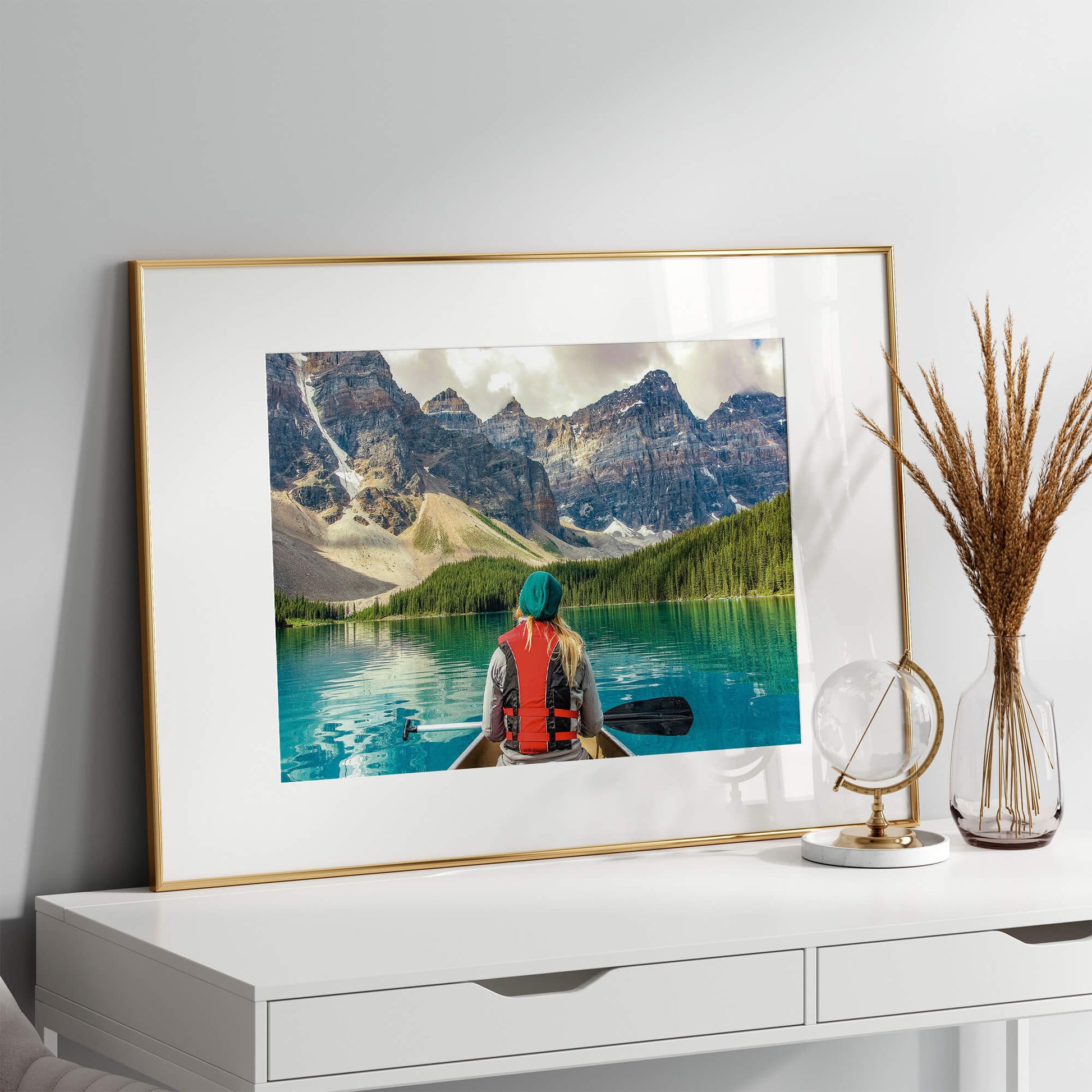 A wooden-framed version of the Mountain Canoeing Print standing on a desk with natural light streaming in.