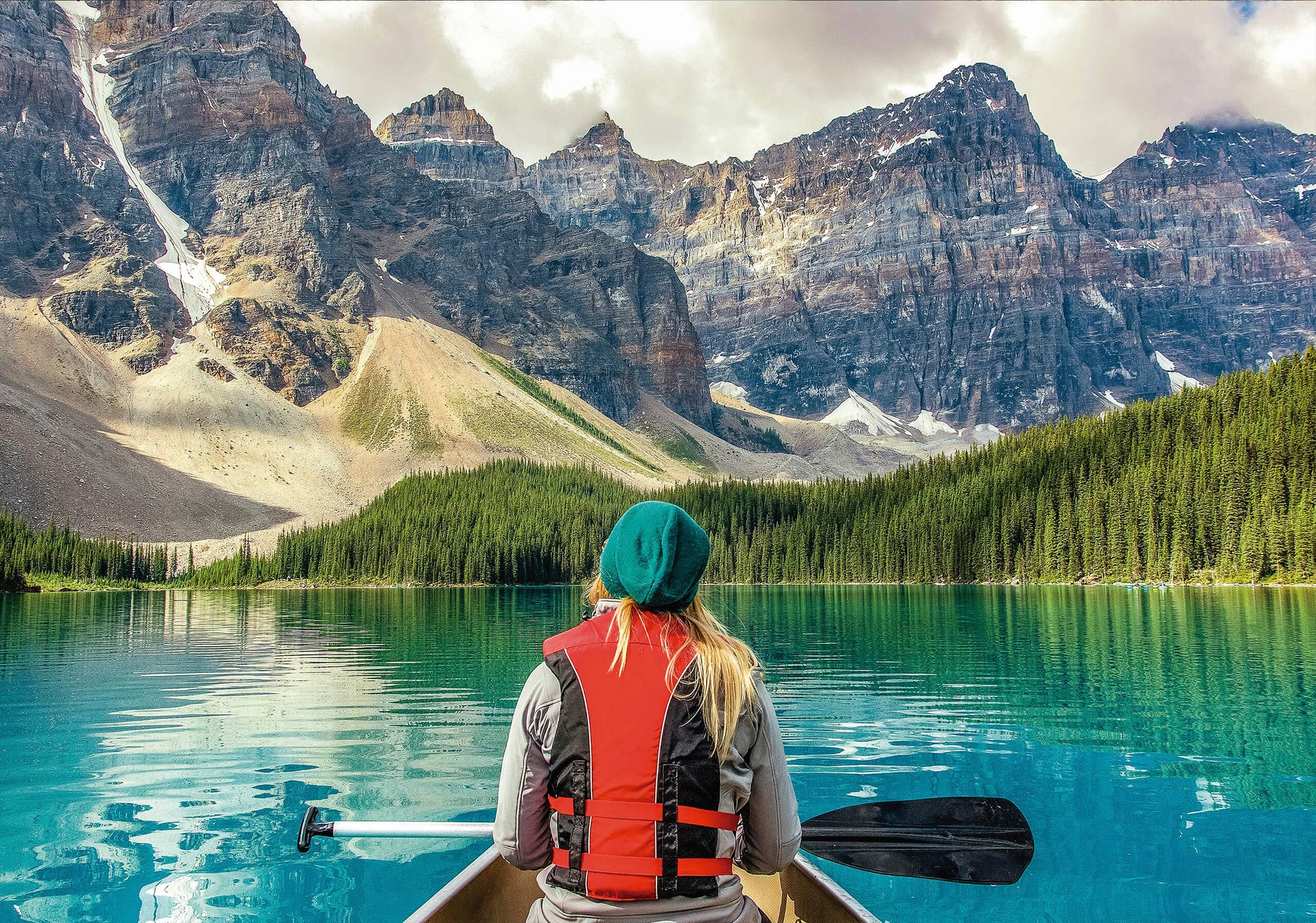 A breathtaking art print featuring a woman canoeing on a turquoise mountain lake, surrounded by towering peaks and lush pine forests.