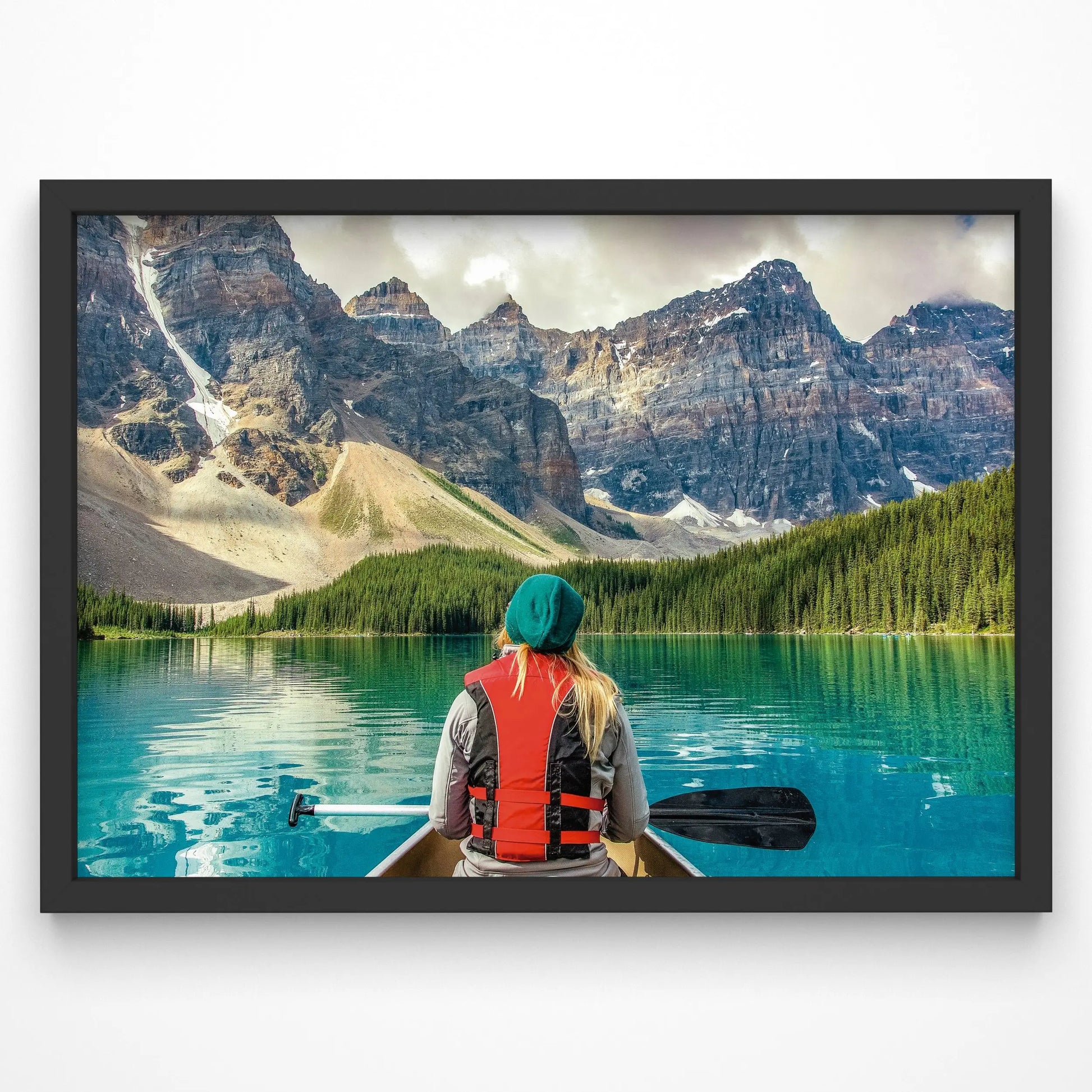 A breathtaking art print featuring a woman canoeing on a turquoise mountain lake, surrounded by towering peaks and lush pine forests.