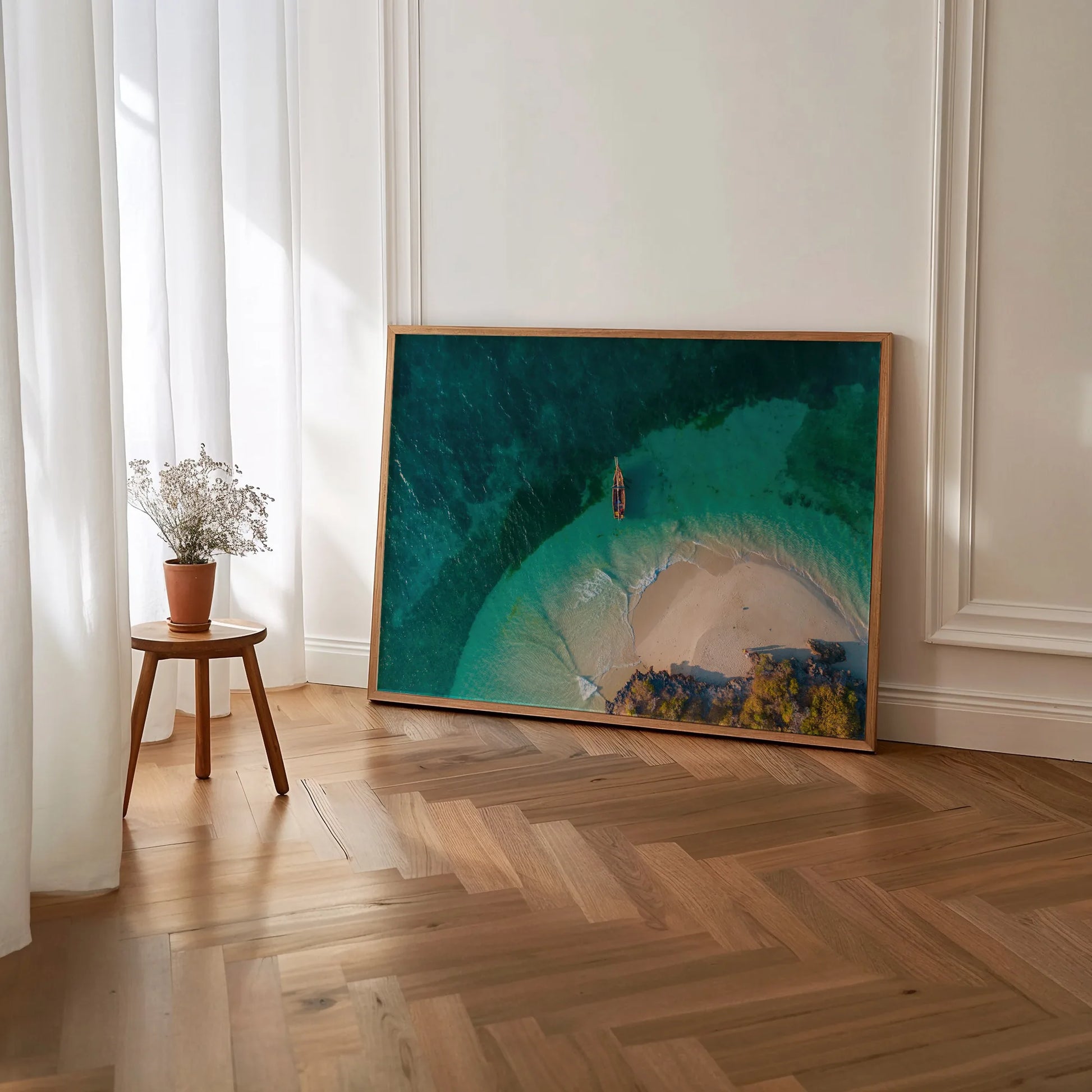 A framed art print featuring a serene beach with a traditional wooden boat anchored near the shore, captured from a high perspective.