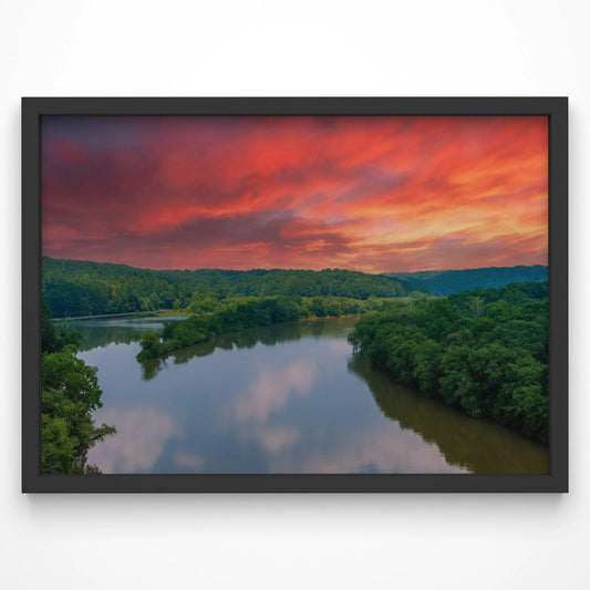 A breathtaking view of a winding river surrounded by lush greenery, set against a dramatic sunrise sky painted in deep oranges and reds. The water reflects the morning light, creating a peaceful and atmospheric landscape.