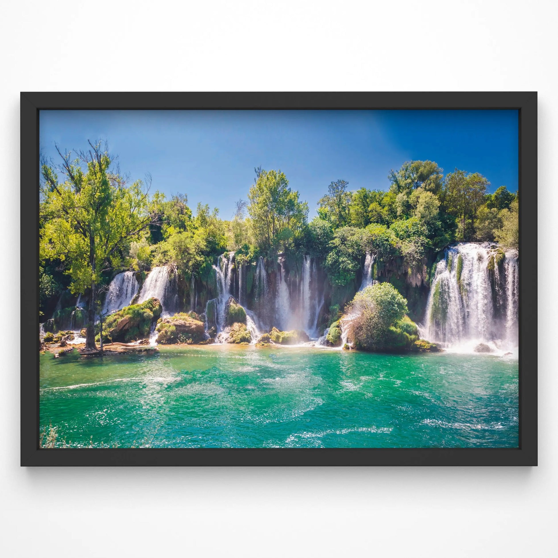 A stunning waterfall cascades into a turquoise pool, surrounded by lush green trees under a clear blue sky.
