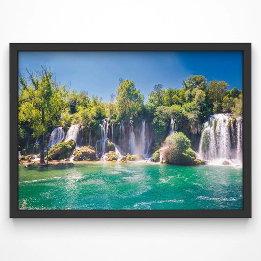 A stunning waterfall cascades into a turquoise pool, surrounded by lush green trees under a clear blue sky.