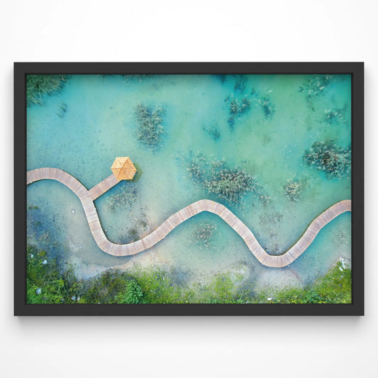 A stunning aerial view of a winding wooden boardwalk meandering over shallow turquoise waters, surrounded by lush greenery.