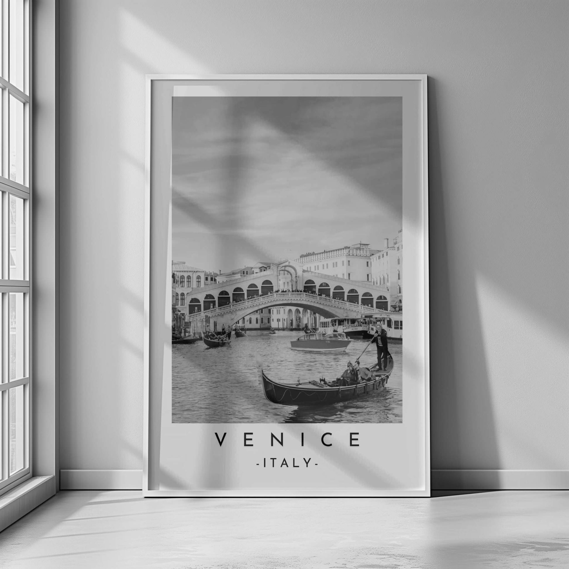 Monochrome photograph of the Rialto Bridge in Venice, Italy, with gondolas navigating the Grand Canal.

